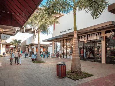 Vista parcial do Porto Belo Outlet Premium, mostrando lojas, com pessoas passeando pelo corredor ao ar livre e uma palmeira decorando o centro.